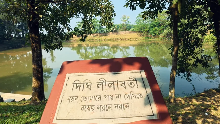 Best Resorts for Couples in Gazipur, Dhaka 27 Plaque Of Dighi Lilaboti Beside A Calm Pond At Nuhash Polli, Gazipur, Bangladesh, Surrounded By Trees And Natural Greenery With A Reflective Water Surface.