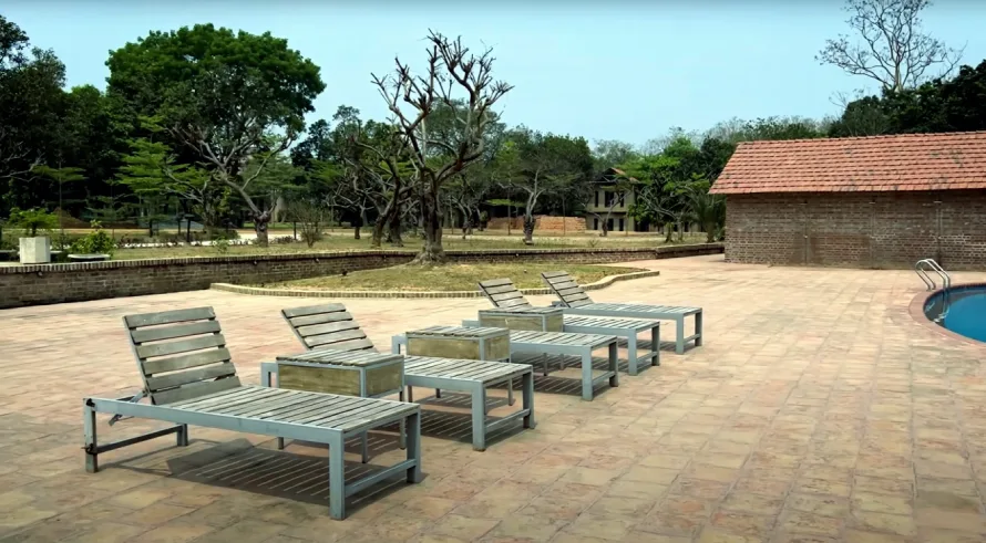 Best Resorts for Couples in Gazipur, Dhaka 15 A Peaceful Poolside Setting At Matir Maya Eco Resort In Gazipur, Bangladesh, Featuring Modern Wooden Loungers, Brick Walkways, And Rustic Architecture Surrounded By Serene Greenery And Open Natural Space—Perfect For A Relaxing Eco-Friendly Getaway.