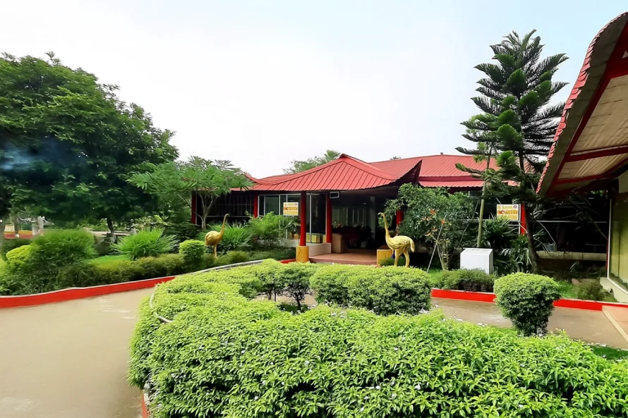 Best Resorts for Couples in Gazipur, Dhaka 2 Front View Of Meghbari Resort In Kaliganj, Gazipur, Featuring Lush Greenery And Traditional Cottages With Red Rooftops.