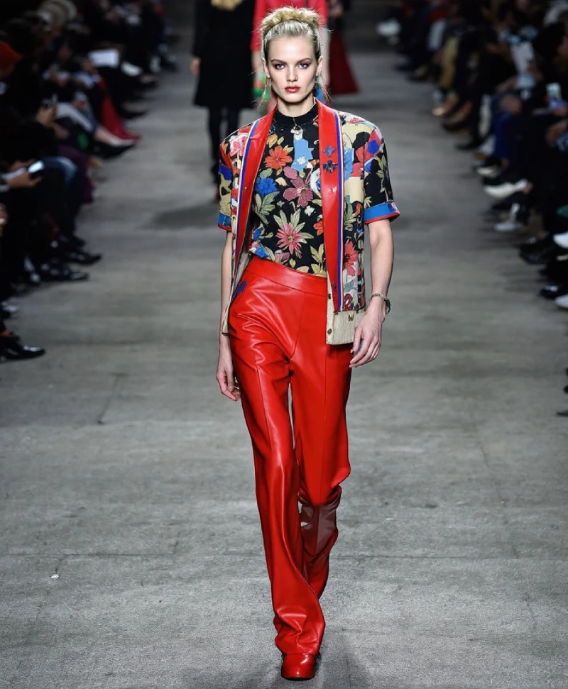 Best Spring Fashion Trends for Every Style in 2025 24 A Model On A Runway Wearing A Vibrant, Short-Sleeved Floral Print Top With A High Collar, Layered Under A Matching Floral Jacket, And Bold Red Wide-Leg Leather Pants. She Has Her Hair In A Bun And Is Wearing Red Shoes, Showcasing A Striking, High-Fashion Look.