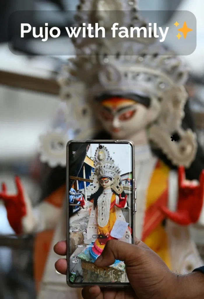 Best Durga Puja Captions, Wishes and Quotes for Social Media 10 A Person Holding A Phone Displaying A Photo Of A Durga Idol, With A Larger, Blurred Durga Idol In The Background And The Text &Quot;Pujo With Family ✨&Quot;.
